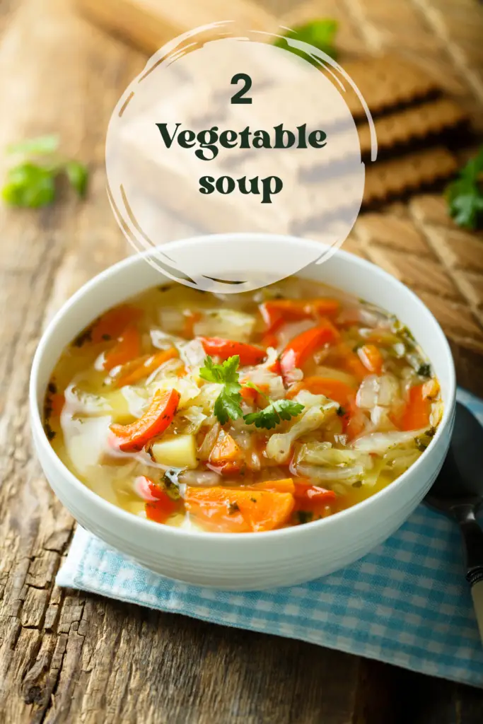 A bowl of homemade vegetable soup with carrots, cabbage, and potatoes, served on a rustic wooden table.