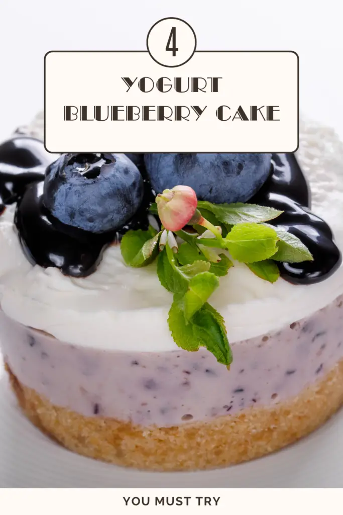 A beautifully plated yogurt blueberry cake topped with fresh blueberries and glossy blueberry sauce.