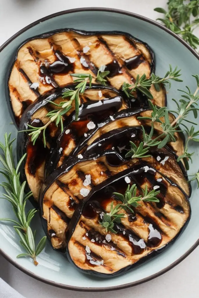 Grilled eggplant slices drizzled with balsamic glaze and garnished with fresh rosemary and coarse sea salt.