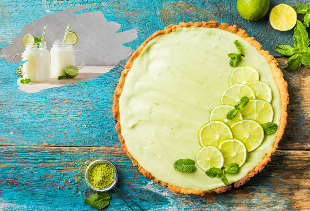 A creamy lime matcha tart decorated with lime slices and mint leaves on a rustic blue table, paired with mason jar lime shakes in the background.