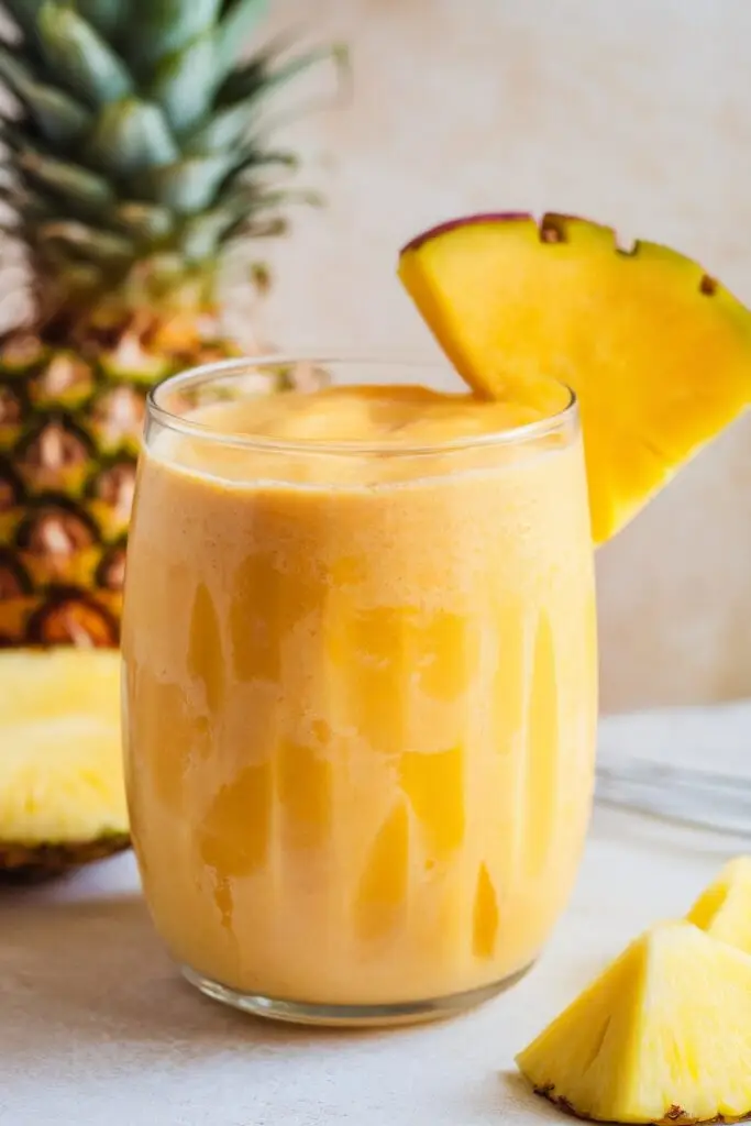 A creamy mango and pineapple smoothie in a glass, garnished with a pineapple wedge.