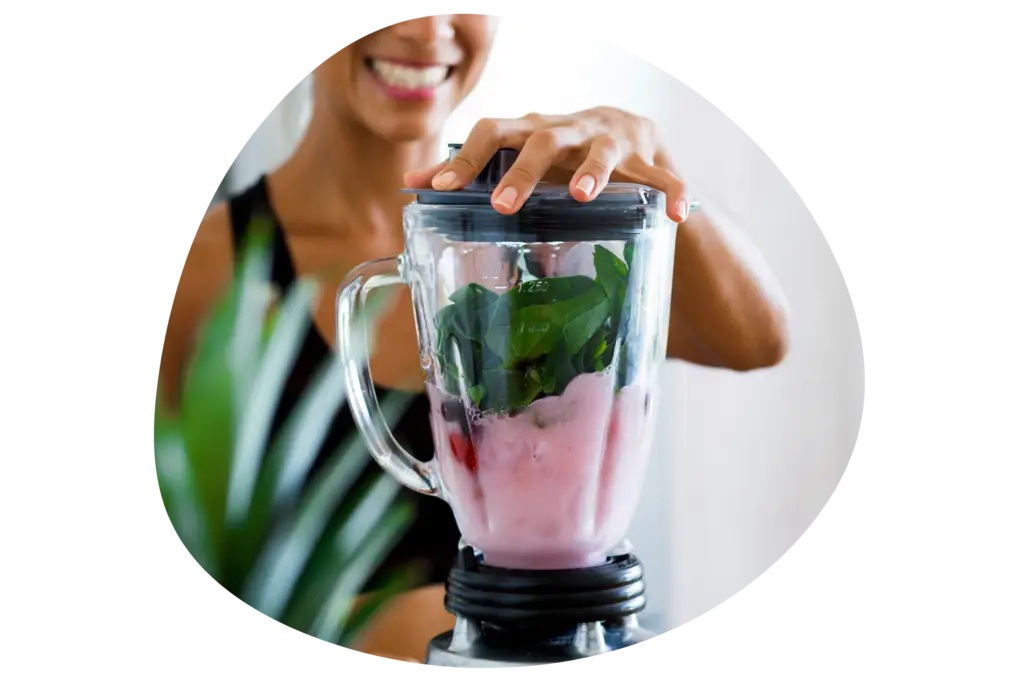 Woman blending a pink smoothie with spinach in a glass blender.