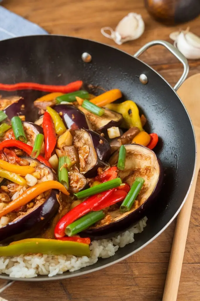 A wok filled with stir-fried eggplant, bell peppers, and green onions tossed in a flavorful sauce.