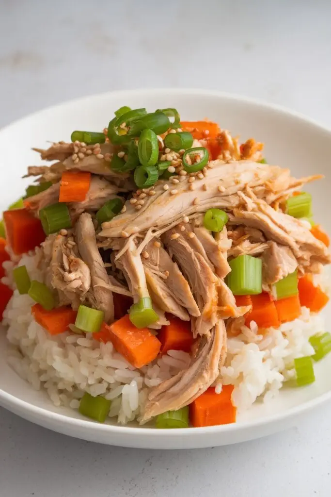 A bowl of shredded chicken, diced carrots, and celery over white rice.