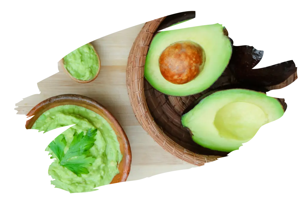 Fresh halved avocado displayed in a woven basket alongside small bowls of creamy avocado spread garnished with parsley, all arranged on a wooden cutting board.