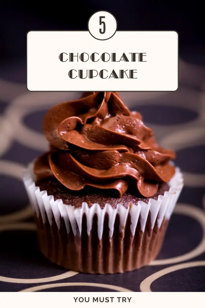 A rich chocolate cupcake with swirled chocolate frosting on a dark background.