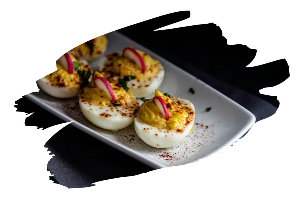 Deviled eggs garnished with thin slices of pink radish and herbs on a white rectangular plate with paprika sprinkled around them against a dark background.