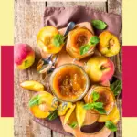 A Mason jar filled with preserved peach slices in syrup, surrounded by fresh whole and halved peaches on a light-colored surface, with a wooden spoon nearby and a warm, softly blurred kitchen background.