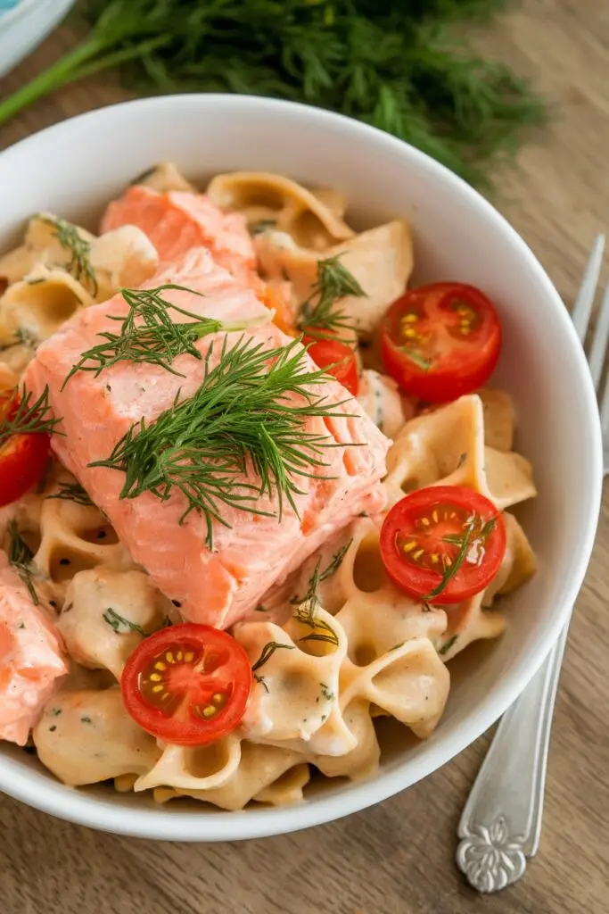 A bowl of creamy pasta topped with poached salmon, cherry tomatoes, and fresh dill.