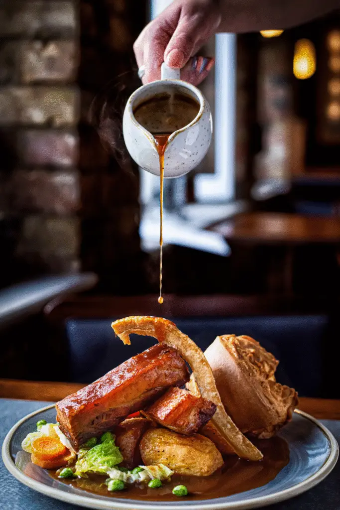 Hearty Sunday Roast meal with roasted pork belly, Yorkshire pudding and vegetables being drizzled with rich gravy in a cozy restaurant setting